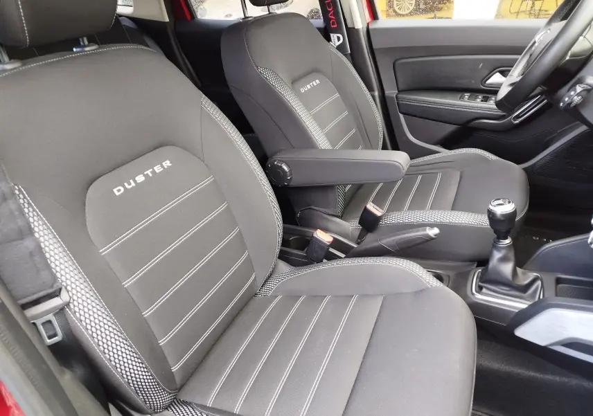 Vue intérieure côté avant droit du Dacia Duster 2020, sièges noirs avec logo Duster brodé et levier de vitesse manuel.