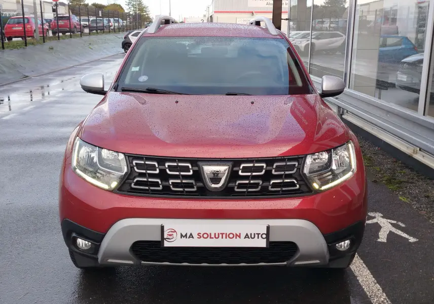 Vue de face d'un Dacia Duster rouge Fusion 2020 avec calandre noire, feux LED allumés et plaque d'immatriculation personnalisée.