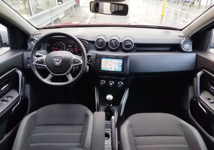 Vue intérieure avant du Dacia Duster 2020 rouge fusion, montrant le volant, la console centrale avec écran tactile et la boîte manuelle.