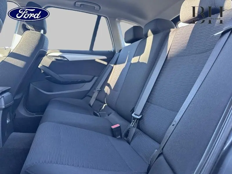 Vue intérieure côté droit sur la banquette arrière noire d'une BMW X1 Mineralgrau avec ceintures de sécurité visibles.