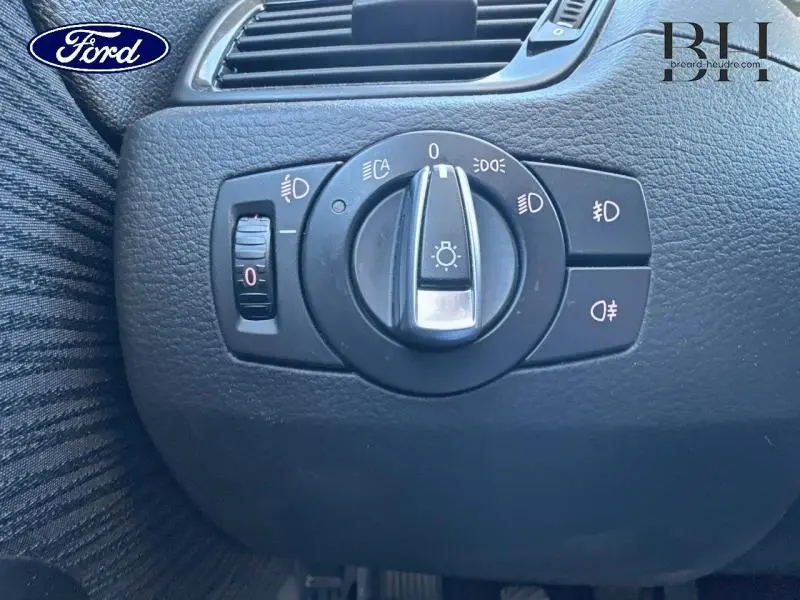 Commande des phares en gros plan sur tableau de bord noir, avec molette centrale et réglage d’intensité lumineuse.