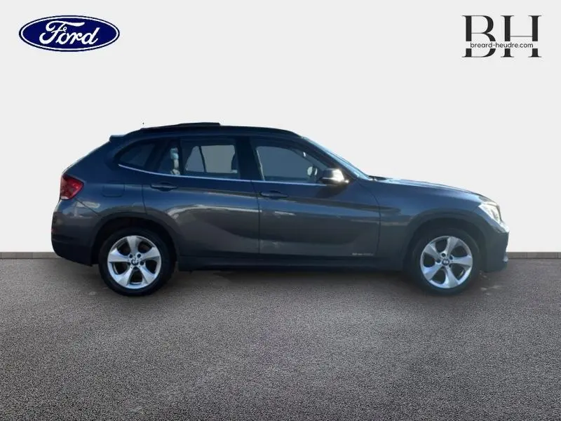 Profil droit d’un BMW X1 Mineralgrau 2013 avec barres de toit noir mat et jantes alu 17 pouces.
