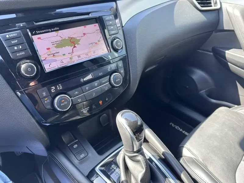 Vue intérieure du tableau de bord et levier de vitesse automatique du Nissan Qashqai blanc, avec écran tactile et commandes climatisation.