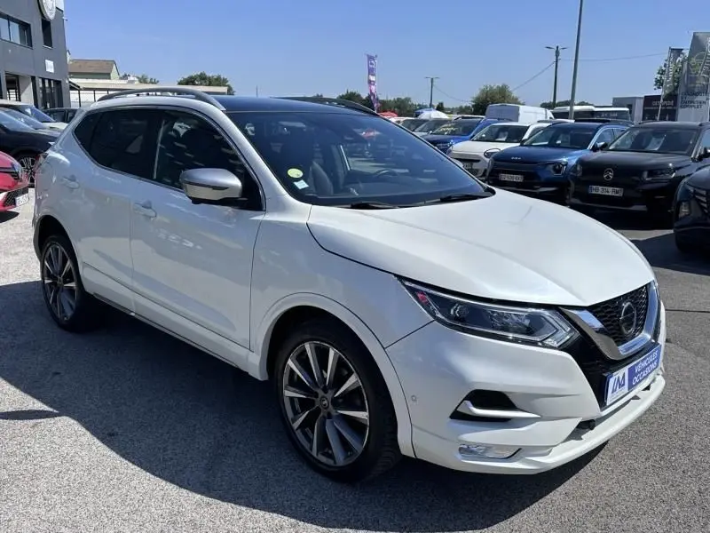 Nissan Qashqai blanc en 3/4 avant droit, avec jantes alliage et calandre chromée, stationné en extérieur.