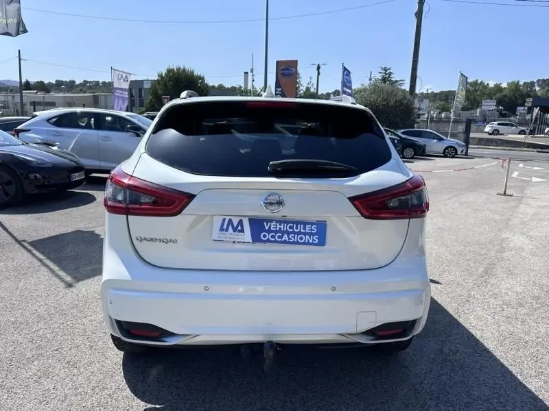 Vue arrière d'un Nissan Qashqai blanc 2019, avec feux arrière rouges et plaque "Véhicules Occasions" visible.