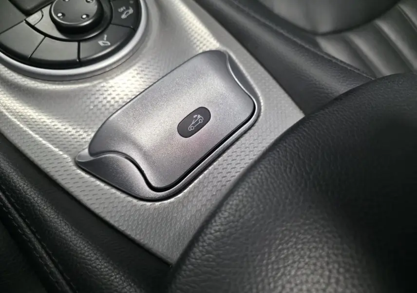 Gros plan sur le bouton d’ouverture du toit rigide dans l’habitacle cuir noir de la Mercedes SL 350 gris.