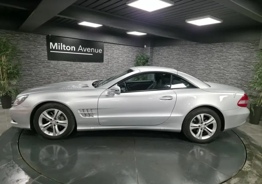 Vue de profil côté gauche d'une Mercedes SL 350 gris métallisé avec toit rigide fermé dans un showroom.