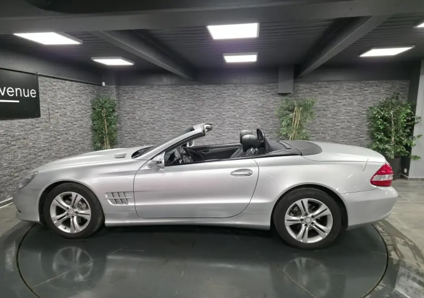 Vue de profil côté gauche d'une Mercedes SL 350 cabriolet gris métallisé avec toit rigide escamotable ouvert.