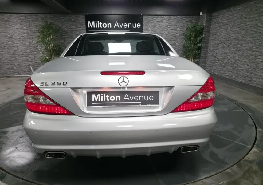 Vue arrière d'une Mercedes SL 350 gris clair, avec feux rouges allumés et double sortie d'échappement chromée.