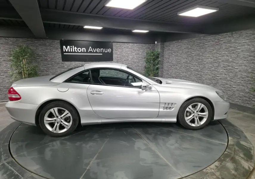Vue de profil côté gauche d'une Mercedes SL 350 gris métallisé avec toit rigide fermé dans un showroom.
