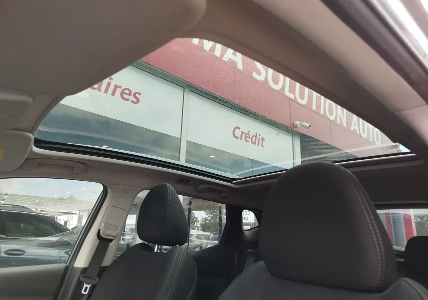Vue intérieure du Nissan Qashqai 2021 avec toit panoramique ouvert et sièges avant en tissu noir.