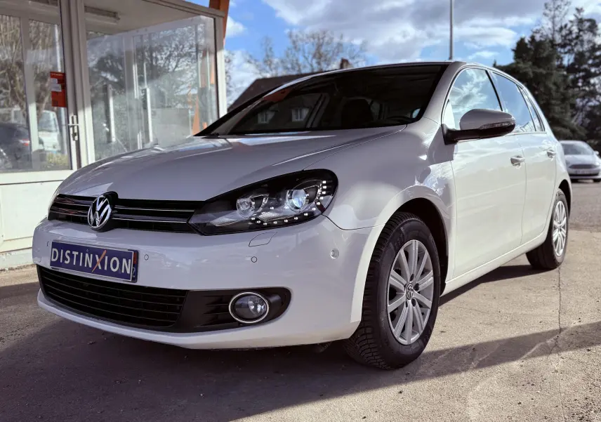 Volkswagen Golf blanc vue 3/4 avant droit avec phares allumés et jantes alliage en extérieur.