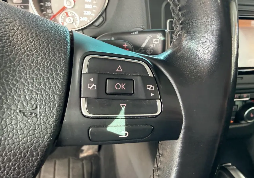 Gros plan sur les commandes multifonctions du volant en cuir noir d'une Volkswagen Golf blanche de 2012.