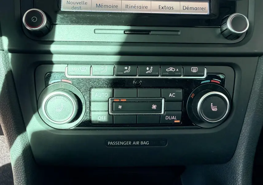 Gros plan sur la console centrale noire de la Volkswagen Golf blanche 2012, montrant les commandes de climatisation et chauffage.