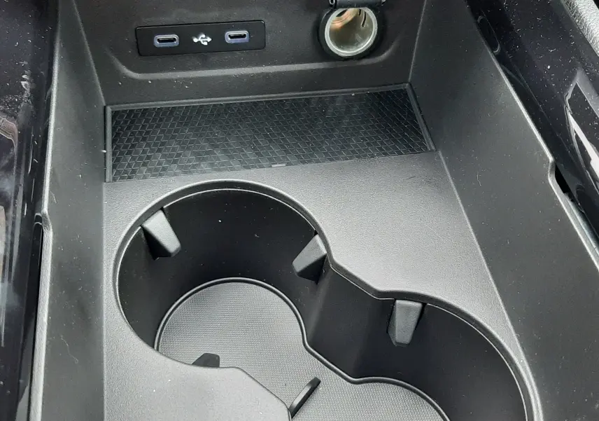 Gros plan sur la console centrale noire du Renault Austral Ph.2 avec porte-gobelets, prises USB et allume-cigare.