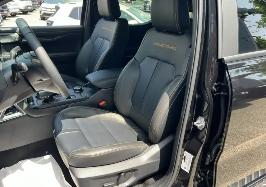 Vue intérieure côté conducteur du Ford Ranger Wildtrak Plus noir agate, sièges cuir avec surpiqûres orange et logo Wildtrak brodé.