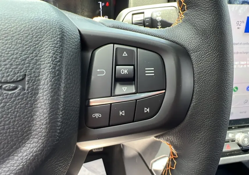Gros plan sur les commandes multifonctions du volant cuir noir du Ford Ranger Wildtrak Plus 2026, avec surpiqûres orange.