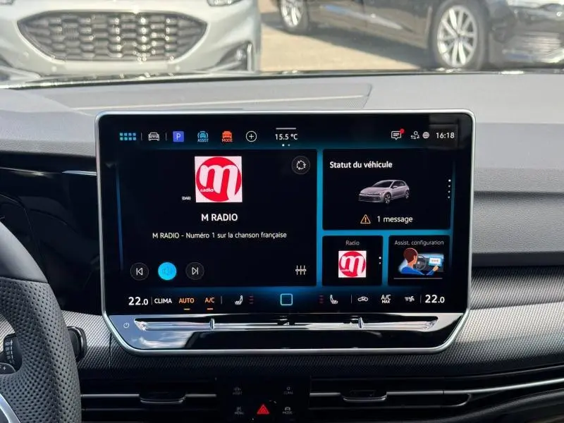 Écran tactile central allumé dans l'habitacle d'une Volkswagen Golf gris lunaire, affichant la radio et le statut du véhicule.