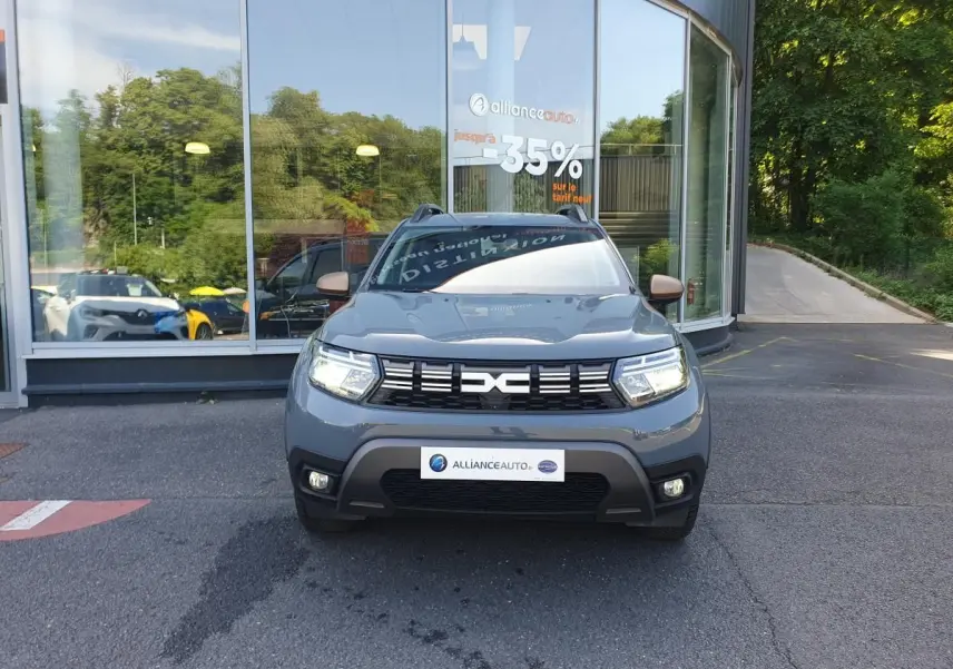 Dacia Duster gris urbain vue de face, avec calandre noire et signature lumineuse LED allumée.