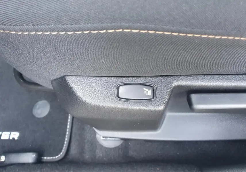 Détail du bouton de siège chauffant sur la partie inférieure d’un siège avant du Dacia Duster gris urbain 2023.