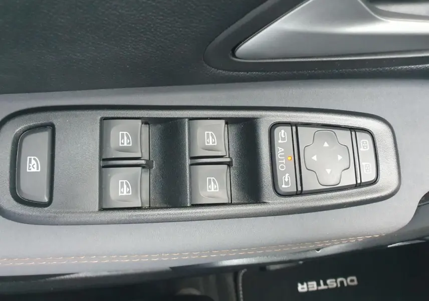 Gros plan sur les commandes des vitres électriques et rétroviseurs sur la porte côté conducteur du Dacia Duster gris urbain 2023.