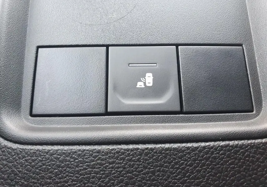 Gros plan sur le bouton de l'avertisseur d'angles morts dans l'habitacle noir du Dacia Duster gris urbain.