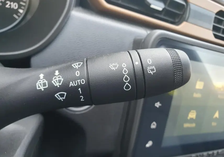 Gros plan sur la commande d’essuie-glace du Dacia Duster gris urbain, avec tableau de bord et écran tactile en arrière-plan.