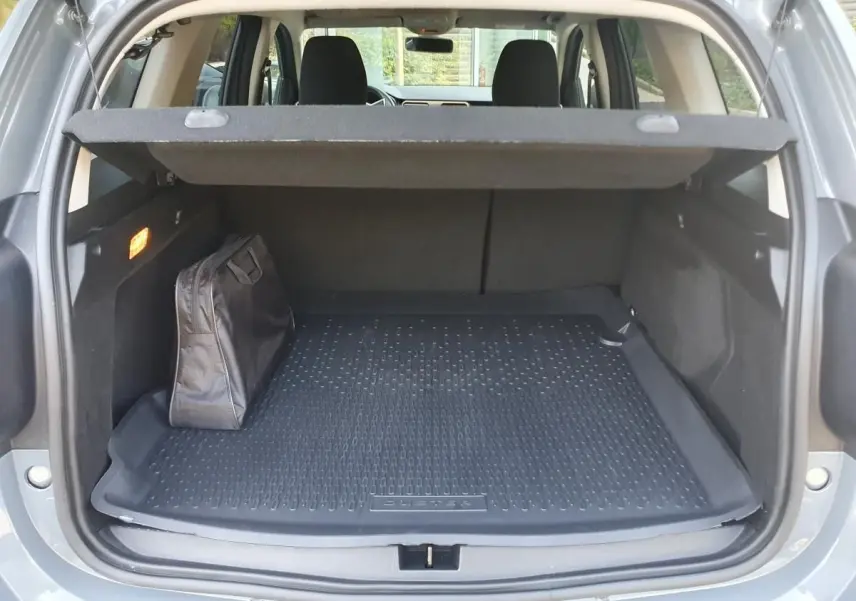 Coffre ouvert du Dacia Duster gris urbain 2023, avec tapis de protection et sac noir à gauche.