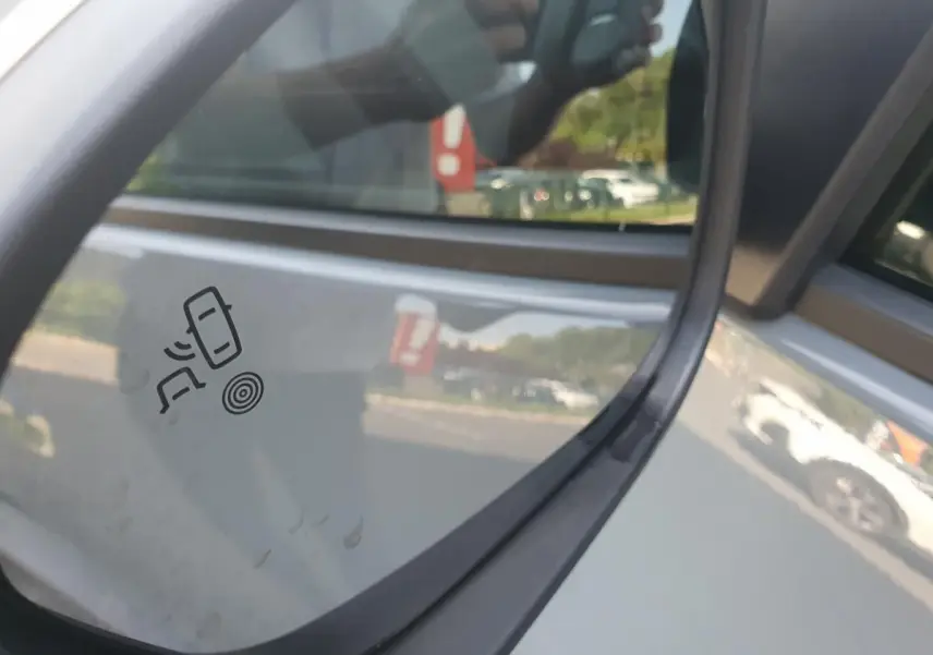 Gros plan sur le rétroviseur droit gris urbain du Dacia Duster 2023 avec pictogramme d’alerte d’angle mort visible.
