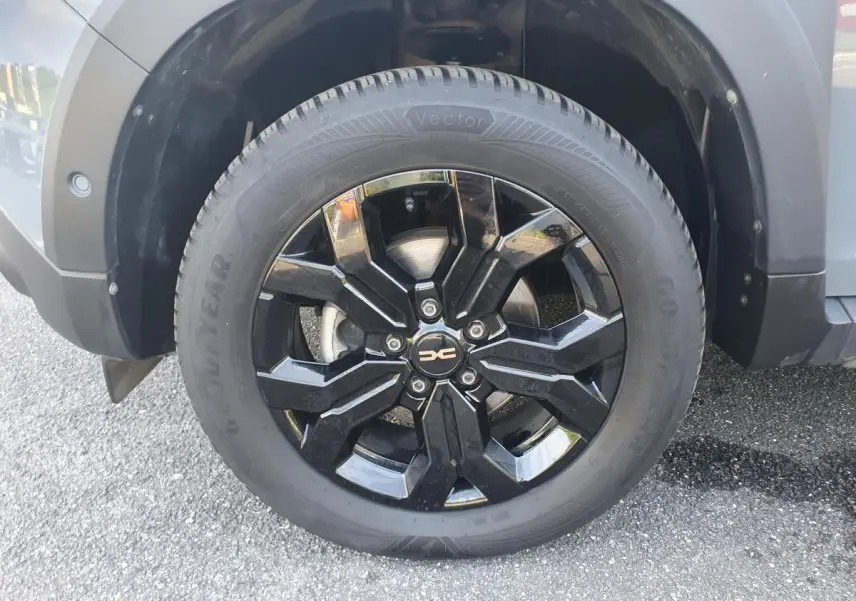 Gros plan sur la roue avant droite du Dacia Duster gris urbain, jante noire brillante au design moderne.