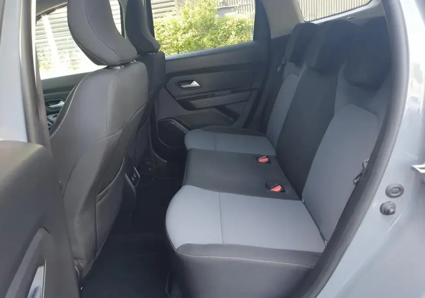 Vue intérieure côté droit des sièges arrière gris clair et foncé du Dacia Duster 2023, porte ouverte sur extérieur lumineux.