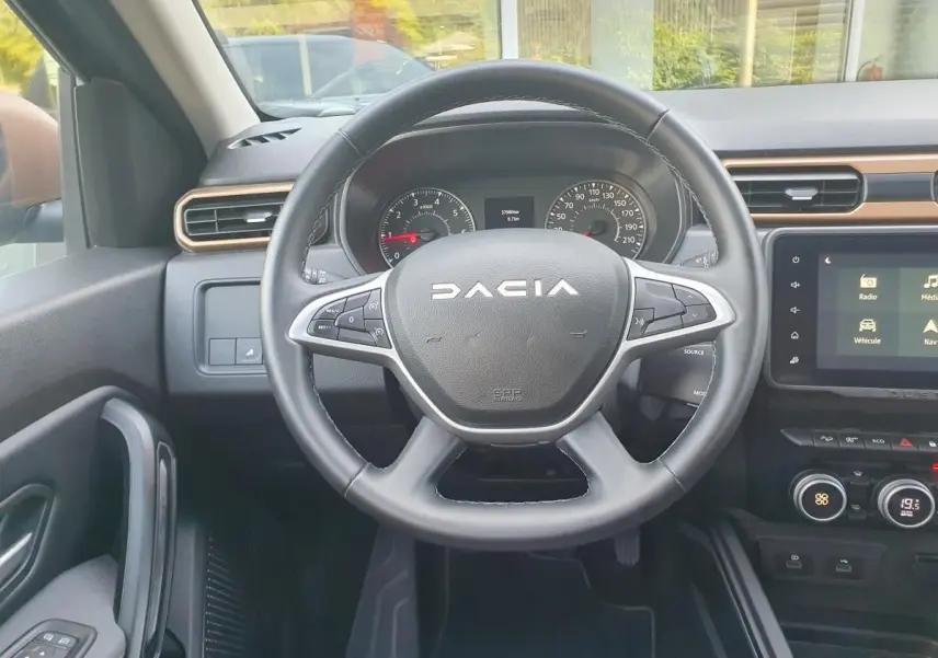 Vue intérieure centrée sur le volant DACIA du Duster 2023 avec tableau de bord et écran tactile visible.