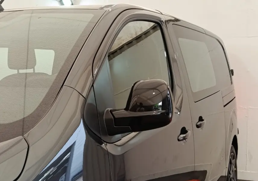 Vue de côté droit avant d’un Citroën Jumpy gris foncé avec vitres teintées et rétroviseur noir brillant.