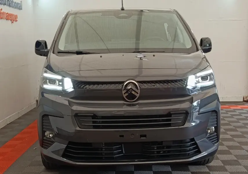Vue frontale d'un Citroën Jumpy gris foncé 2025 avec phares LED allumés dans un showroom.