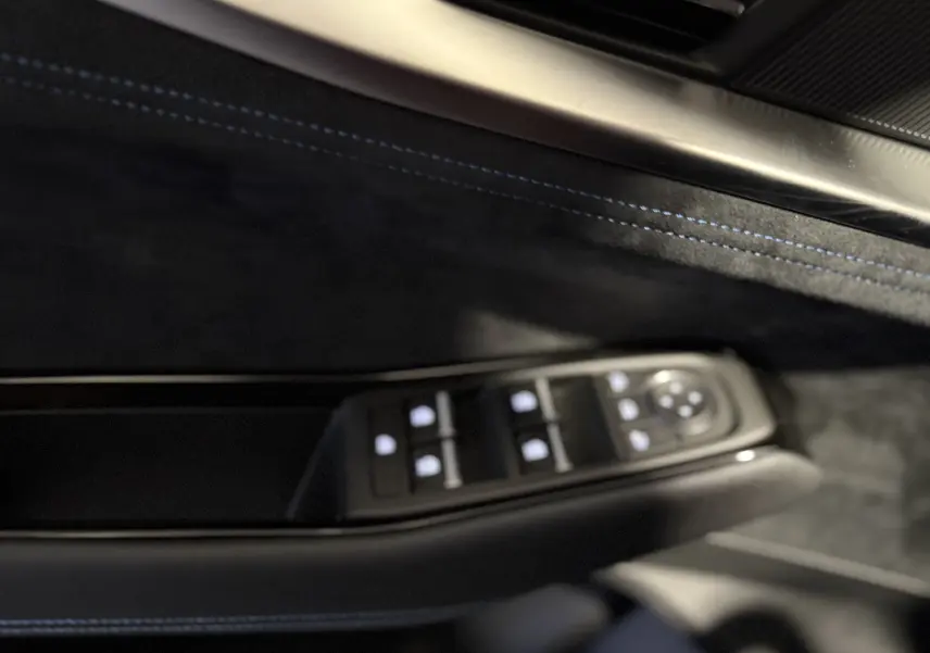 Gros plan sur la commande des vitres côté conducteur du Renault Austral blanc nacré, avec surpiqûres bleues sur la garniture intérieure noire.