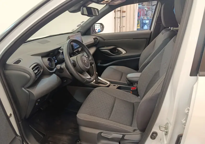 Intérieur côté conducteur d'une Toyota Yaris Cross blanche, sièges gris et tableau de bord avec écran tactile.