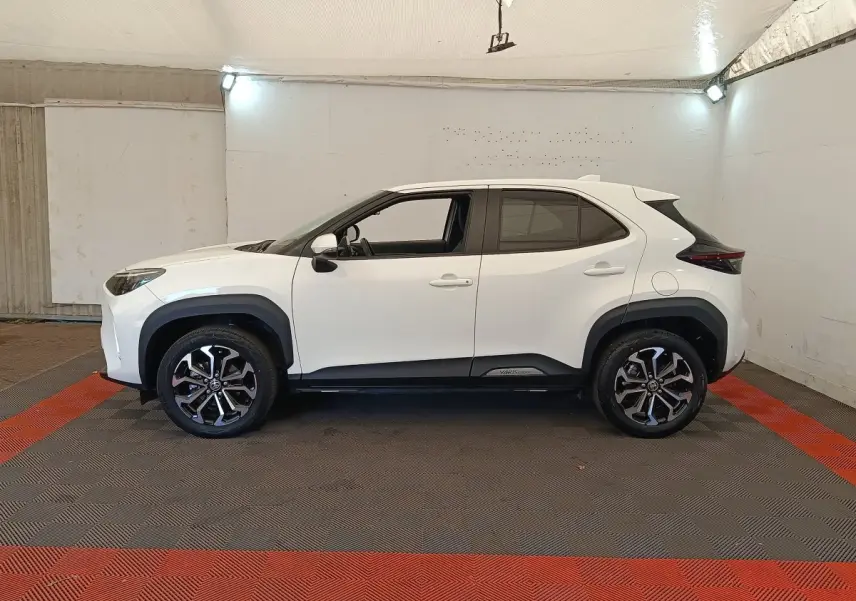 Profil droit d'un Toyota Yaris Cross blanc 2022 avec jantes alliage noires et détails noirs contrastants sous un éclairage intérieur.