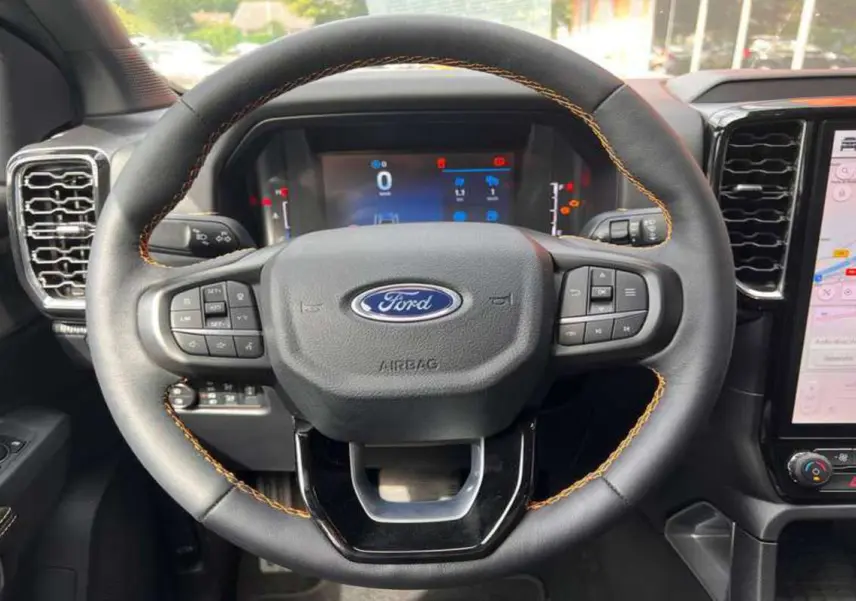 Vue rapprochée du volant cuir noir avec surpiqûres orange du Ford Ranger 2026, tableau de bord digital et écran tactile visibles.