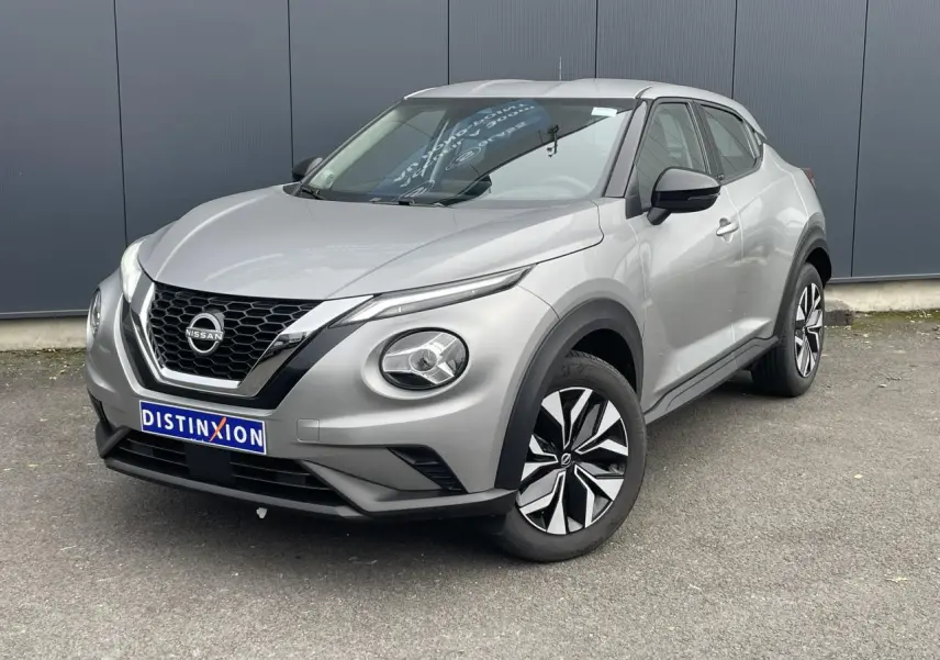 Nissan Juke gris silver en 3/4 avant droit, avec calandre noire et jantes bicolores distinctives.