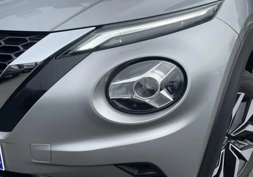 Gros plan sur le phare avant droit et la calandre d’un Nissan Juke 2024 gris silver avec jante alliage visible.