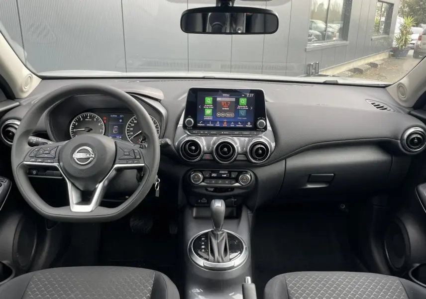 Vue frontale de l'habitacle noir du Nissan Juke 2024 avec volant multifonction et écran tactile central.