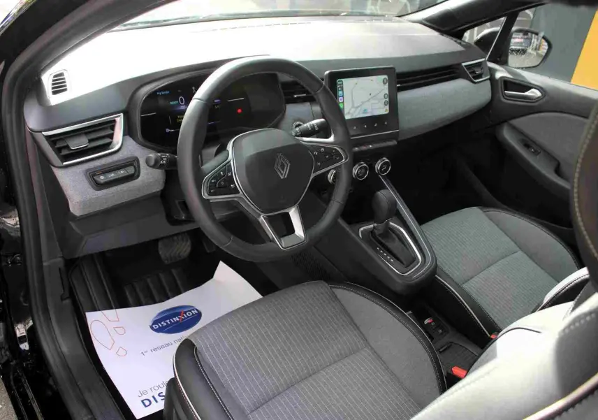Vue intérieure côté conducteur de la Renault Clio 2025 hybride, volant multifonction et écran tactile central gris noir.