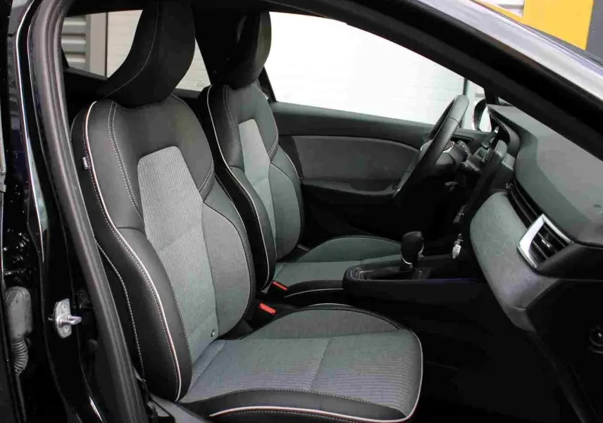 Vue intérieure côté conducteur de la Renault Clio noire étoile métal, sièges tissu gris noir avec surpiqûres blanches.
