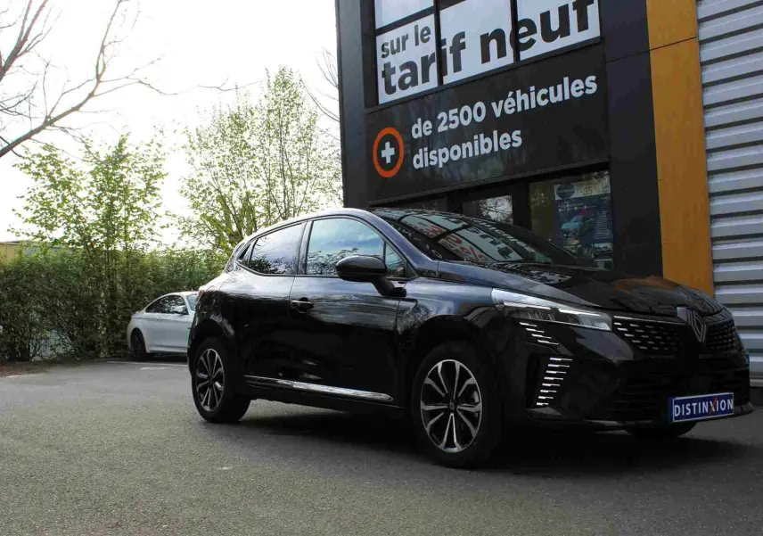 Renault Clio noire étoile métal vue 3/4 avant droit, avec feux LED et jantes alliage distinctives, stationnée devant un panneau publicitaire.