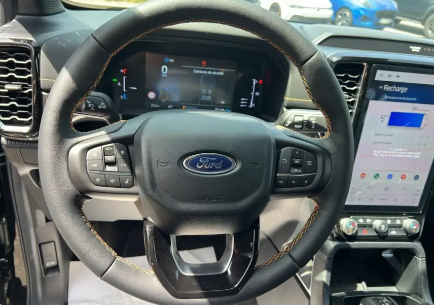 Vue rapprochée du volant cuir noir avec surpiqûres jaunes du Ford Ranger 2025, écran numérique et console tactile visibles.