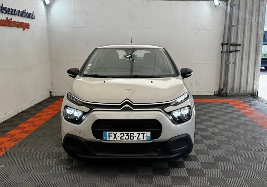 Citroën C3 beige vue de face en intérieur, avec phares LED allumés et calandre noire distinctive.