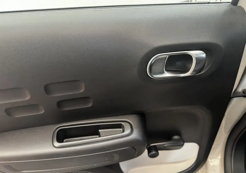 Vue rapprochée de la porte intérieure côté droit de la Citroën C3 beige, avec poignée argentée et manivelle de vitre.