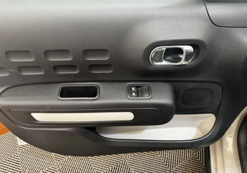 Vue rapprochée de la porte avant droite beige de la Citroën C3 avec poignée intérieure chromée et commandes de vitres.