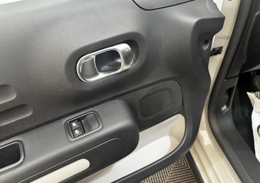 Vue rapprochée de la porte avant gauche beige d'une Citroën C3 2021 avec poignée intérieure chromée et commandes de vitres.