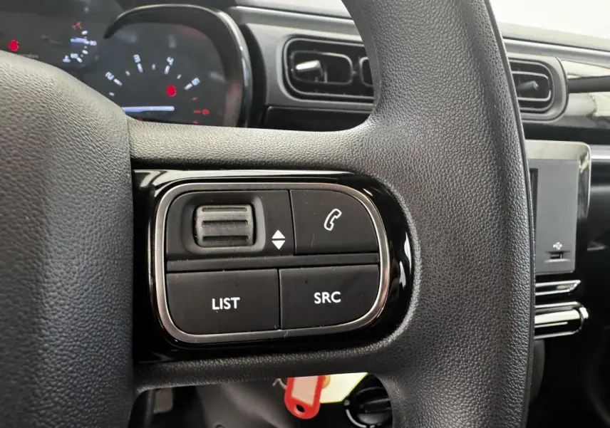 Gros plan sur les commandes du volant noir de la Citroën C3 beige, avec tableau de bord et écran tactile en arrière-plan.